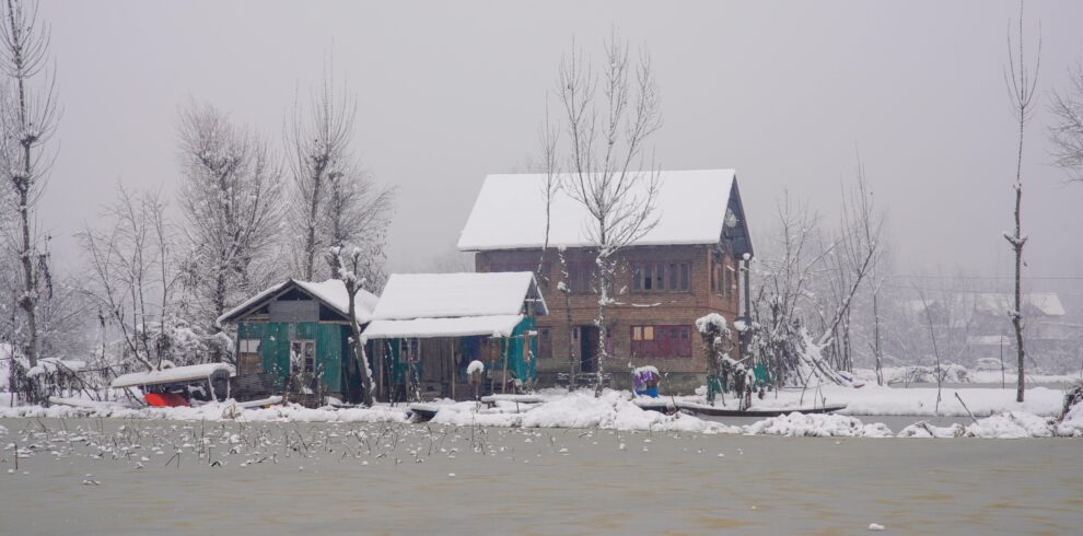 A serene winter scene of snow-covered homes by a lake in Kashmir.